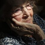 Eine alte Frau stützt ihr Gesicht in ihre Handfläche.